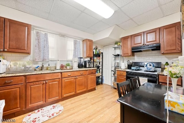 kitchen featuring decorative backsplash, brown cabinetry, light wood-style floors, gas range oven, and under cabinet range hood