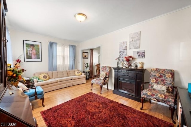 living area with ornamental molding, wood finished floors, and a glass covered fireplace