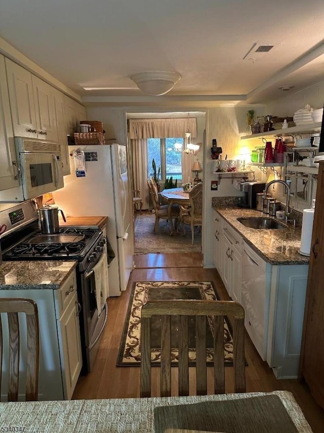 kitchen with white appliances, wood finished floors, stone counters, white cabinetry, and a sink