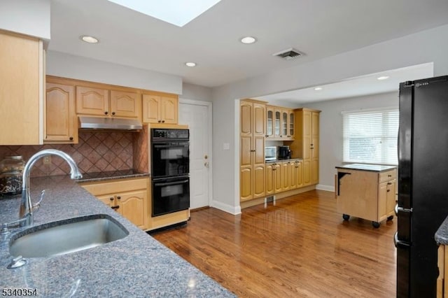 kitchen featuring light brown cabinets, a sink, wood finished floors, under cabinet range hood, and black appliances