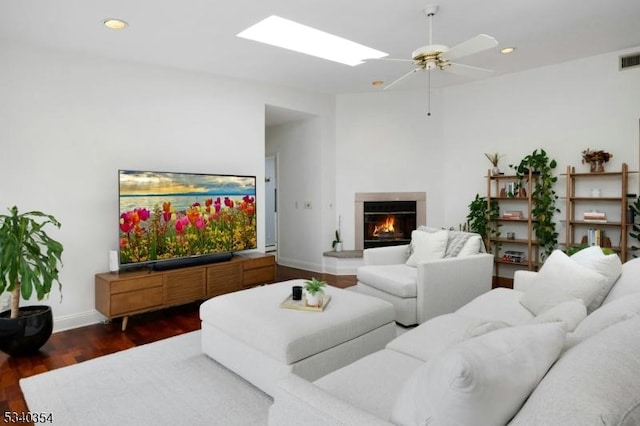 living area featuring a warm lit fireplace, a skylight, baseboards, dark wood-style flooring, and recessed lighting