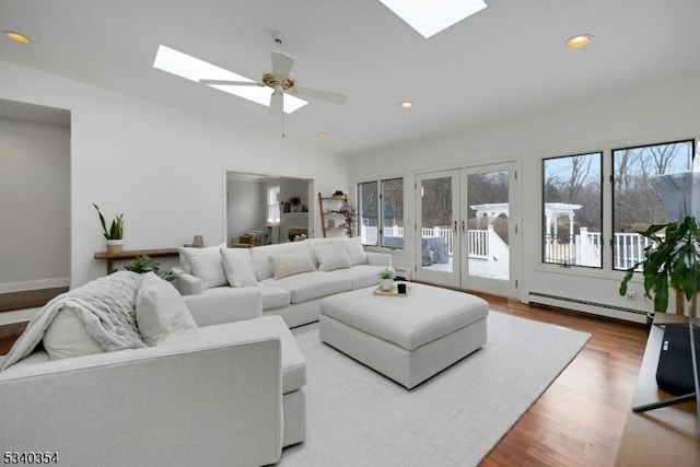 living room featuring recessed lighting, a baseboard heating unit, a ceiling fan, wood finished floors, and vaulted ceiling with skylight