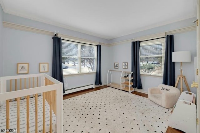 bedroom with a nursery area, a baseboard heating unit, wood finished floors, and ornamental molding