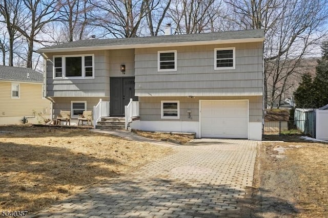 bi-level home with decorative driveway, fence, and an attached garage