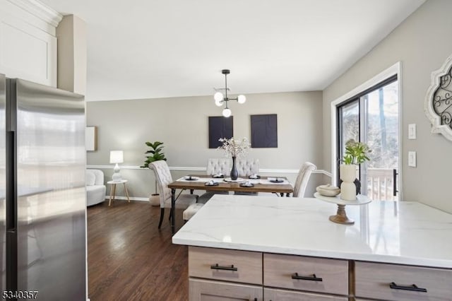 kitchen featuring light stone counters, decorative light fixtures, dark wood-type flooring, stainless steel fridge, and baseboards