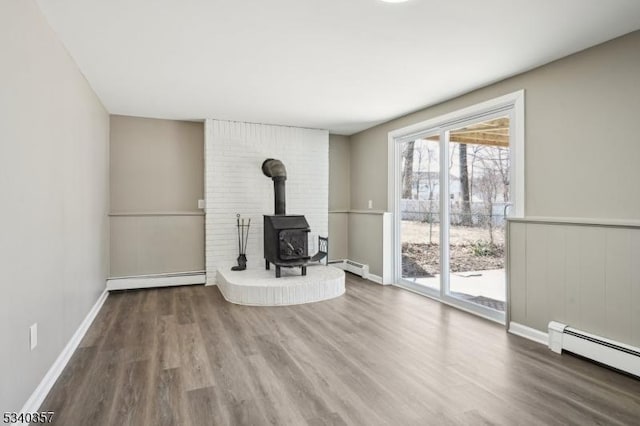 unfurnished living room with a wood stove, a baseboard radiator, a baseboard heating unit, and wood finished floors