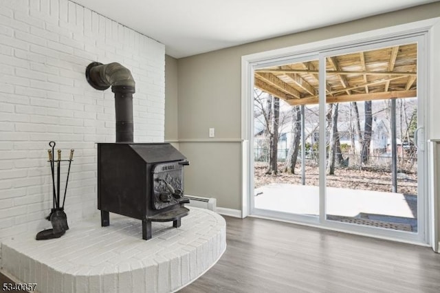 interior space featuring a wood stove, plenty of natural light, baseboard heating, and wood finished floors