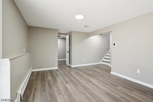 spare room with baseboard heating, stairway, baseboards, and wood finished floors