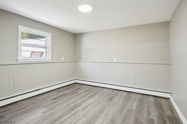 unfurnished room featuring a baseboard heating unit, wood finished floors, and wainscoting