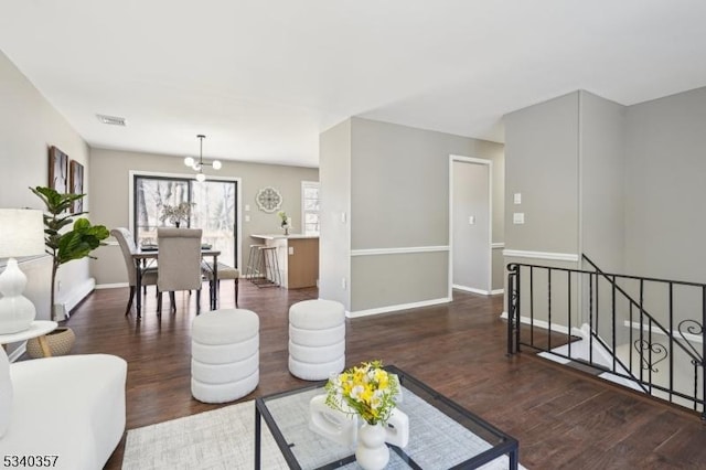 living room featuring an inviting chandelier, visible vents, baseboards, and wood finished floors