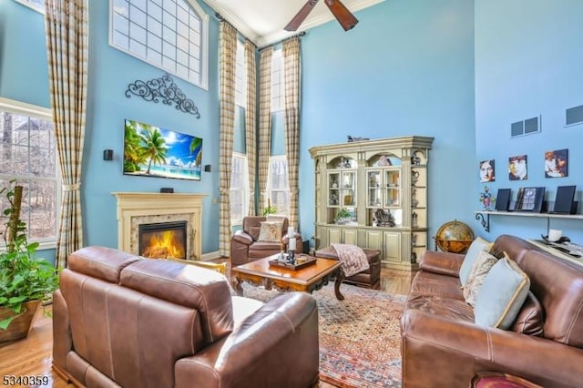 living room featuring visible vents, ornamental molding, wood finished floors, a high end fireplace, and a towering ceiling