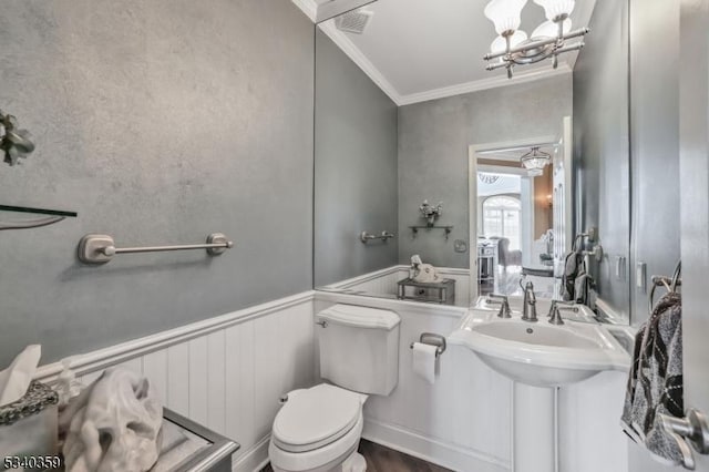 half bath featuring visible vents, a wainscoted wall, crown molding, toilet, and a chandelier