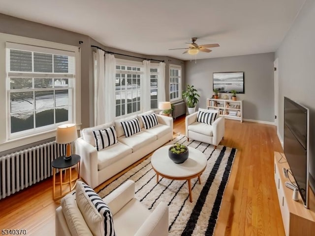 living room with light wood-style floors, radiator, baseboards, and a ceiling fan