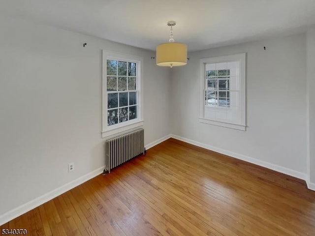 unfurnished room featuring a healthy amount of sunlight, hardwood / wood-style flooring, radiator heating unit, and baseboards