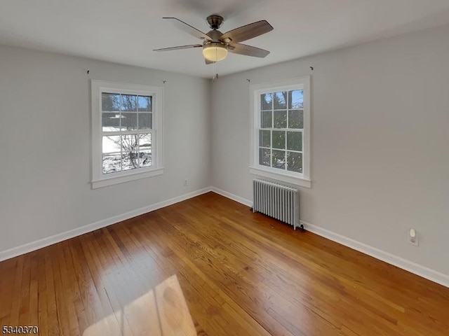 unfurnished room featuring radiator, a healthy amount of sunlight, baseboards, and hardwood / wood-style flooring