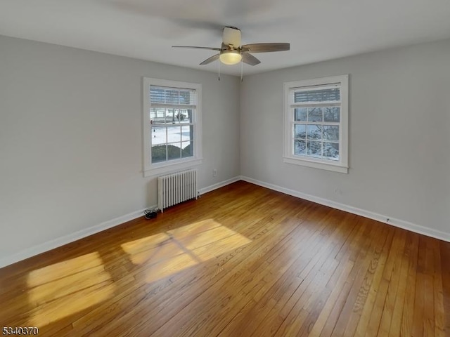 spare room with baseboards, ceiling fan, wood-type flooring, and radiator