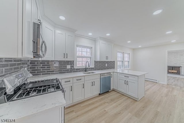 kitchen featuring white cabinets, appliances with stainless steel finishes, a peninsula, a baseboard heating unit, and a sink