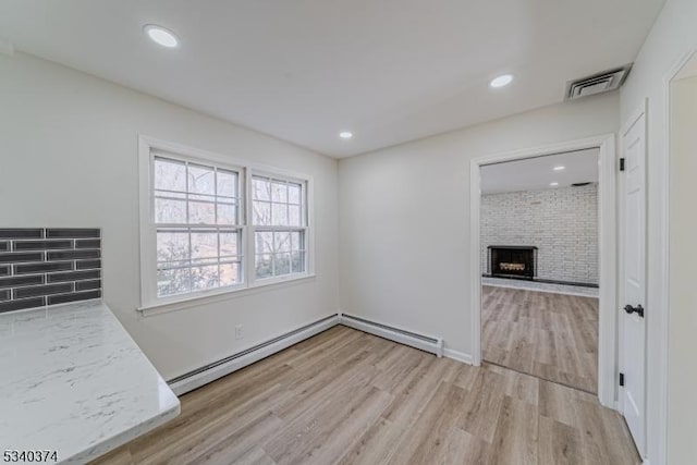 interior space featuring recessed lighting, visible vents, a baseboard heating unit, a brick fireplace, and light wood-type flooring