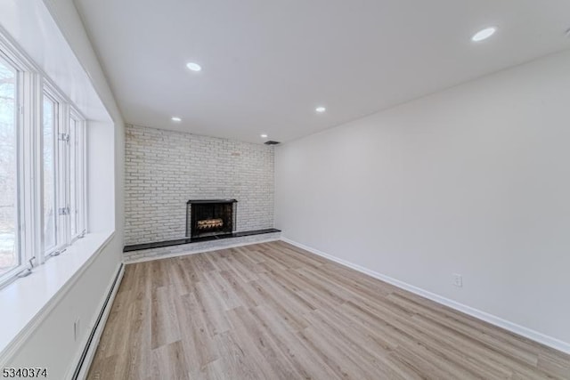 unfurnished living room featuring baseboards, a brick fireplace, light wood-style flooring, and a healthy amount of sunlight