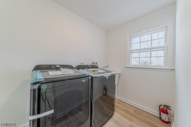 clothes washing area featuring light wood-type flooring, washer and dryer, laundry area, and baseboards