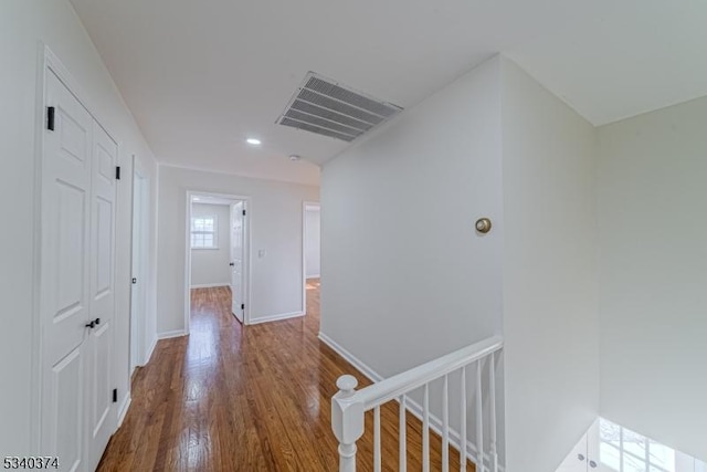 hallway featuring baseboards, visible vents, wood finished floors, and an upstairs landing