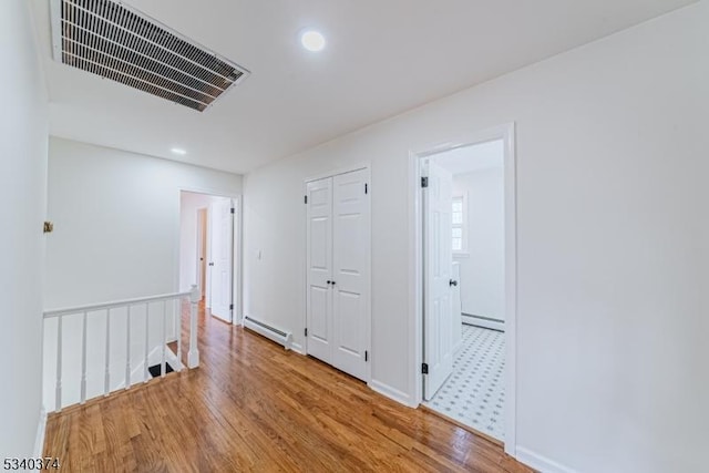 corridor featuring visible vents, baseboard heating, a baseboard heating unit, light wood-style floors, and an upstairs landing