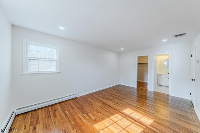 empty room featuring light wood-style flooring, visible vents, baseboard heating, and baseboards