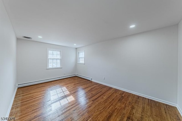 unfurnished room featuring baseboard heating, wood finished floors, visible vents, and baseboards