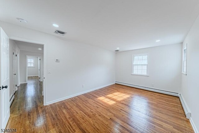 spare room with baseboards, visible vents, a baseboard radiator, wood finished floors, and baseboard heating