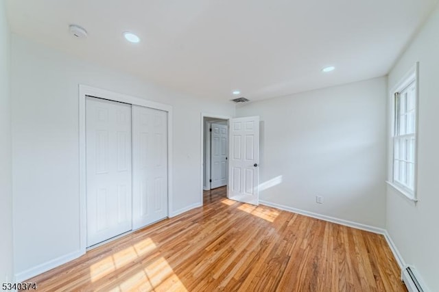 unfurnished bedroom with a baseboard radiator, baseboards, light wood-style flooring, and a closet