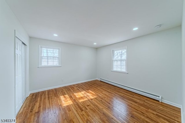 unfurnished bedroom with a baseboard radiator, recessed lighting, wood finished floors, baseboards, and a closet