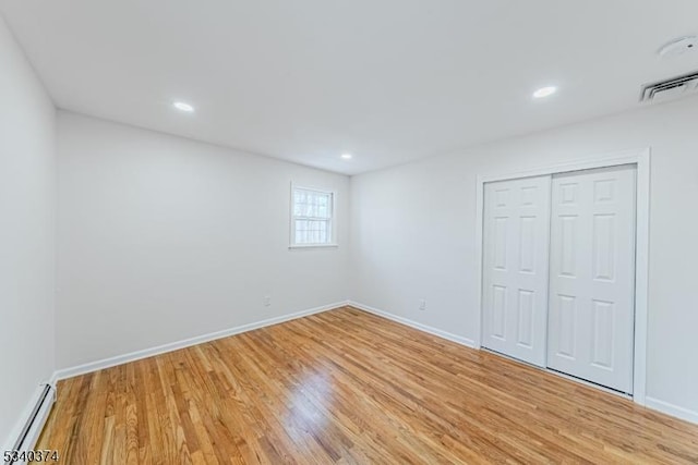 unfurnished bedroom featuring light wood-style floors, baseboards, baseboard heating, and a closet