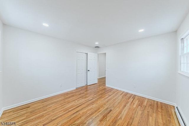 unfurnished room featuring light wood-style flooring, a baseboard heating unit, baseboards, and recessed lighting