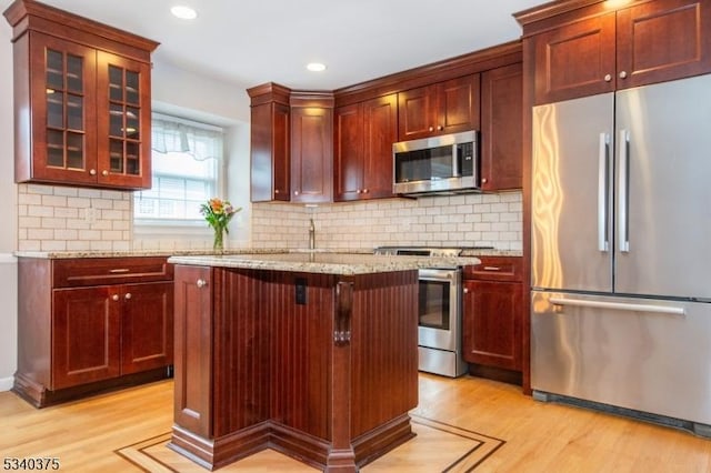 kitchen with stainless steel appliances, light wood-type flooring, light stone counters, and dark brown cabinets