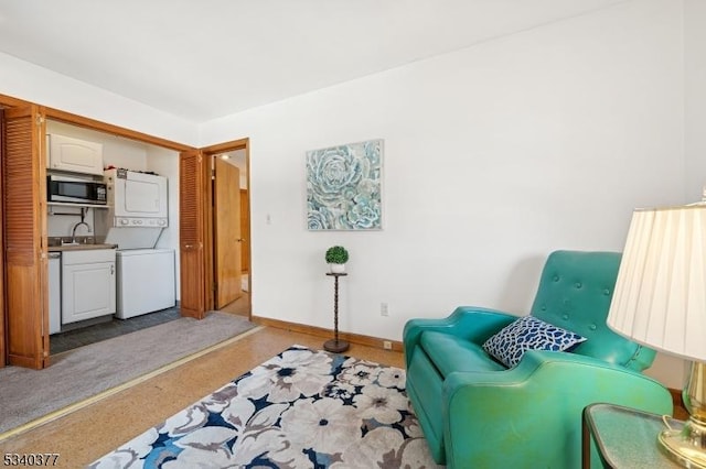 sitting room featuring baseboards, stacked washer / dryer, and light colored carpet