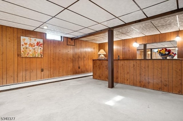 basement with a paneled ceiling, wood walls, and a baseboard radiator