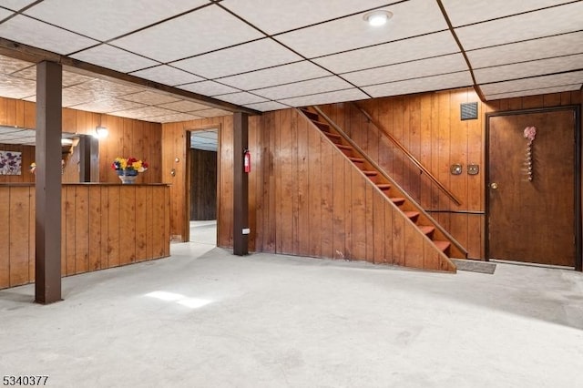 finished basement featuring stairway, a drop ceiling, and wooden walls