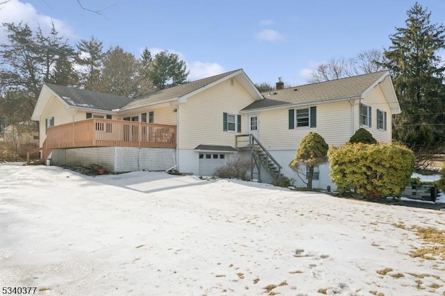 snow covered property featuring a wooden deck, a chimney, and an attached garage