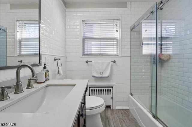 bathroom with tile walls, bath / shower combo with glass door, radiator, toilet, and wood finished floors