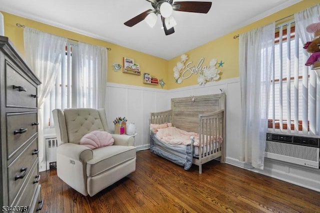 bedroom with radiator, ceiling fan, dark wood-style flooring, and wainscoting