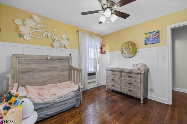 bedroom with dark wood-type flooring, wainscoting, a ceiling fan, and a decorative wall