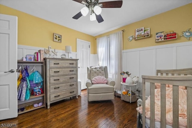 bedroom with a wainscoted wall, dark wood finished floors, a ceiling fan, and a decorative wall