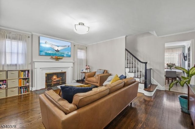 living area with stairs, dark wood-style flooring, a brick fireplace, and a healthy amount of sunlight