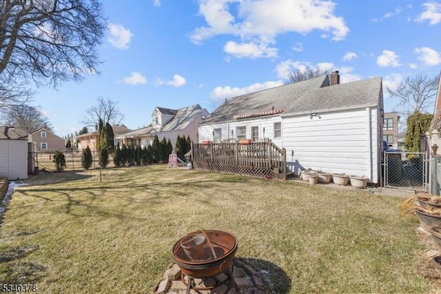 back of property with an outdoor fire pit, fence, a deck, and a lawn