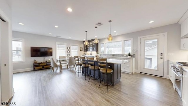 kitchen with recessed lighting, white cabinets, a kitchen breakfast bar, light wood-type flooring, and stainless steel range