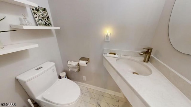 half bathroom featuring marble finish floor, toilet, vanity, and baseboards