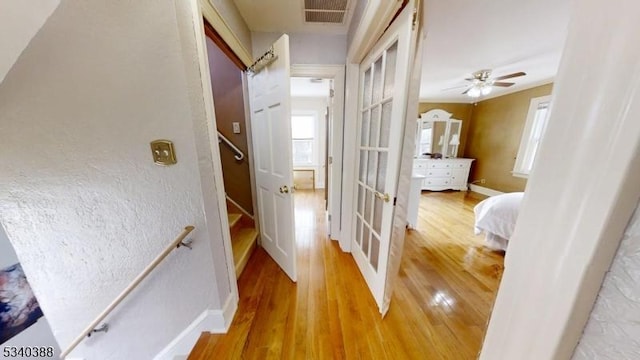 hall with baseboards, visible vents, wood finished floors, and an upstairs landing