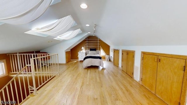 unfurnished bedroom featuring vaulted ceiling with skylight, light wood-style flooring, recessed lighting, and two closets