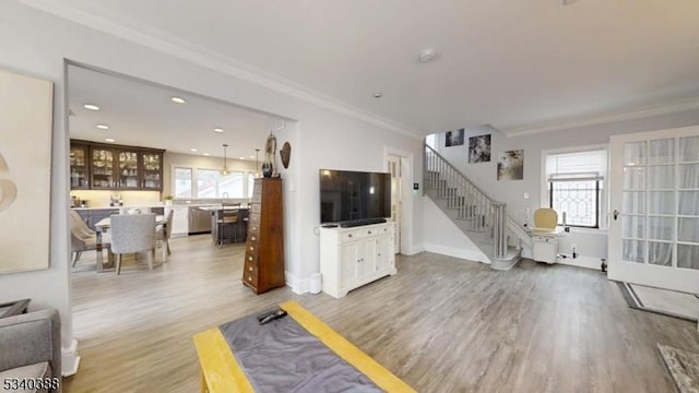 living room featuring light wood-type flooring, stairway, a wealth of natural light, and ornamental molding