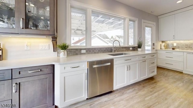 kitchen with light wood finished floors, stainless steel dishwasher, a sink, and a healthy amount of sunlight